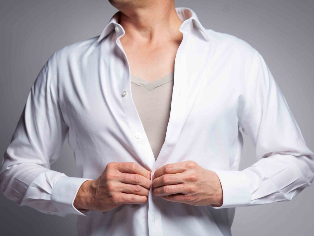 Man buttoning up a white shirt over a heather grey v-neck undershirt